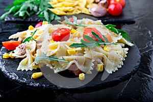 Pasta salad in slate plate with tomatoes cherry, tuna, corn and arugula. ingredients. Italian food.