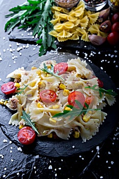 Pasta salad in slate plate with tomatoes cherry, tuna, corn and arugula. ingredients. Italian food.