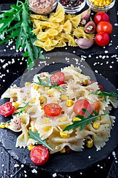 Pasta salad in slate plate with tomatoes cherry, tuna, corn and arugula. Top view. ingredients. Italian food.