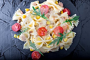 Pasta salad in slate plate with tomatoes cherry, tuna, corn and arugula. Top view. ingredients. Italian food.