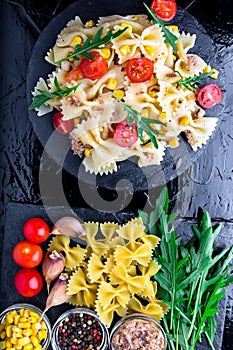 Pasta salad in slate plate with tomatoes cherry, tuna, corn and arugula. Top view. ingredients. Italian food.