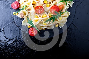 Pasta salad in slate plate with tomatoes cherry, tuna, corn and arugula. Top view. Italian food. Copy space.