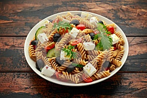 Pasta salad with tomato, black olives, cucumber and feta cheese on wooden table. healthy food.