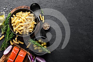 Pasta, salmon fish and ingredients for cooking on black background, top view. Italian food