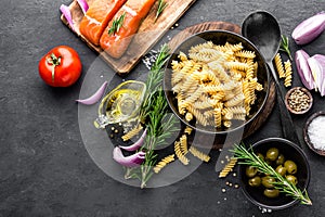 Pasta, salmon fish and ingredients for cooking on black background, top view. Italian food