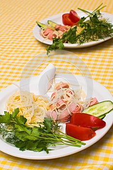 Pasta with sausage and tomatoes with greens on a white plate