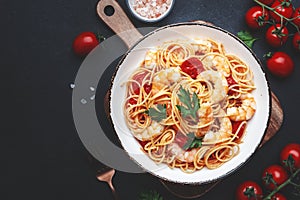 Pasta with shrimp, tomatoe sauce, olive oil and parsley in plate on black table background. Top view, copy space