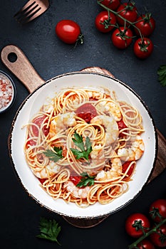 Pasta with shrimp, tomatoe sauce, olive oil and parsley in plate on black table background. Top view, copy space