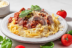 Pasta spaghetti bolognese with minced beef sauce, tomatoes, parmesan cheese and fresh basil in a plate on white table