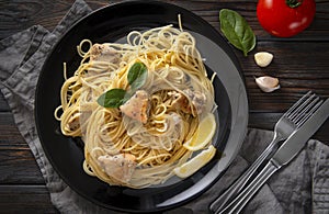 Pasta, spaghetti with chicken fillet, lemon slices, herbs, tomato, garlic, on a black plate on a dark wooden background,  fork,