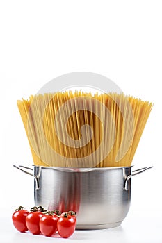 Pasta spaghetti in a metal pan in a large collum on a white background with tomatoes.