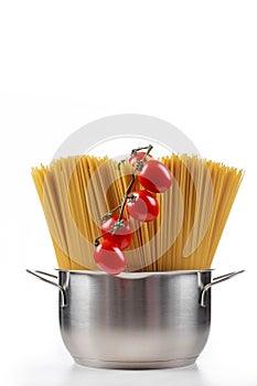 Pasta spaghetti in a metal pan in a large collum on a white background with tomatoes.
