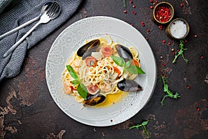 Pasta spaghetti with seafood, shrimps, mussels, tomatoes and basil on dark concrete table top view