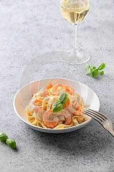 Pasta spaghetti with shrimps, prawn decorated basil and glass of white wine on grey table