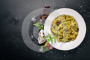 Pasta with spinach, olives and mushrooms with parmesan cheese. Italian food. On a black wooden surface.