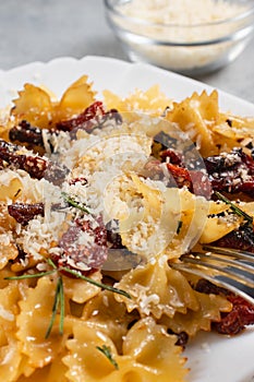 Pasta with sun dried tomatoes and parmesan in a white plate on the table. Italian food dish, vertical image