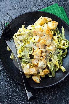 Pasta Tagliatelle in creamy sauce with baked cauliflower in a plate on a dark background. Selective focus.Top view