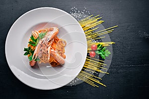 Pasta and tiger shrimp in tomato sauce. Italian traditional food. On a wooden background.