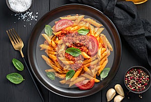 Pasta with tomato bolognese sauce and fresh basil on a black background.