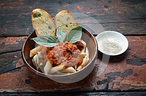 Pasta with tomato sauce, garlic bread and parmesan cheese aside on rustic wooden background