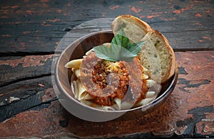 Pasta with tomato sauce with garlic bread on rustic wooden background