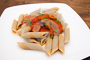 Pasta with tomato sauce and olives on wood close up