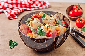 Pasta Tortiglioni with minced meat, tomato sauce and tomatoes in coconut bowl on rustic beige background