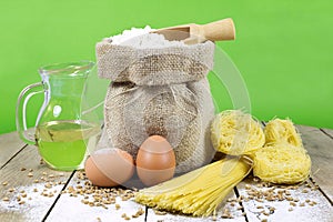 Pasta, Two Eggs, Jute Bag Filled with Flour, Wooden Spoon and Olive Oil in Glass Bottle on an Old Wooden Table