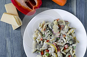 Pasta with vegetables and cheese on a white plate colored background top view