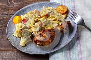 Pasta with vegetables and cherry tomatoes next to a baked chicken leg on the table next to a light napkin and a fork.