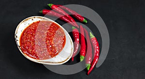 Paste harissa sauce in a bowl on a black background close up. Adjika hot chili peppers sauce. Copy space