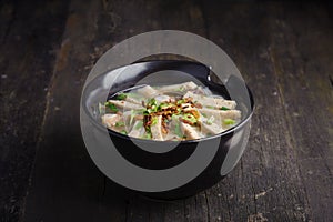 Paste of rice flour with scallion, coriander, deep fried garlic and porks on top in black porcelain bowl