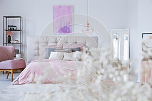 Pastel bedding on king size bed in stylish bedroom interior with abstract pink and purple painting on white wall