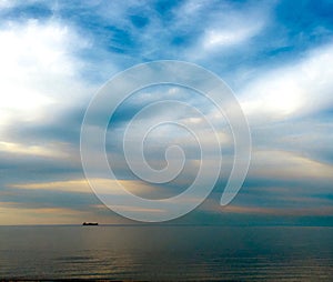 Pastel blue and gold skies on ocean horizon with ship in distance