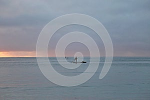 Pastel blue sunset with fisherman silhouette over raft