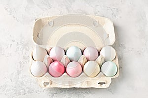 Pastel colored Easter eggs in egg box on light grey background.