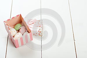 Pastel colored easter eggs in a gift box over white wooden background.