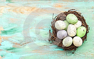 Pastel colored easter eggs in nest on wooden background