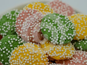 Pastel colored, green, yellow and pink white chocolate mint candies covered in white dot sprinkles piled up close