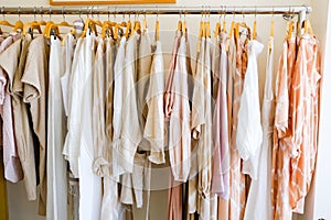 pastel colorful summer collection of natural clothes on hangers in retail fashion shop.
