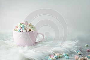 Pastel coloured mini marshmallows in pink cup on fuzzy fur and light grey underground with sprinkles on underground HR SF