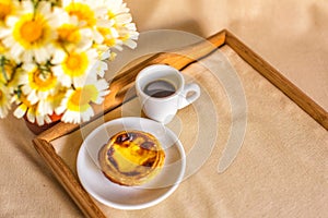 Pastel de nata cake, a cup of Portuguese black coffee and a bouquet of daisies on a tray. Top view