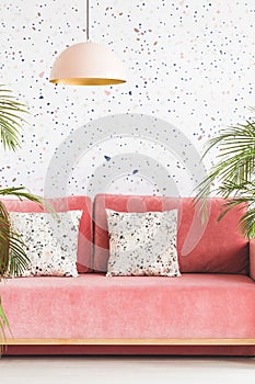 Pastel lamp above pink couch with patterned cushions in living r