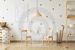 Pastel lamp above table between chairs in gold kid`s room interi