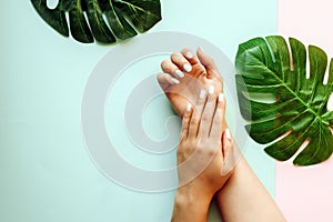 Pastel manicure on a blue and pink background with palm leaves. Tropical background with woman`s hands