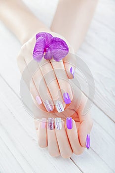 Pastel manicure with orchid on white background. Combination of purple, white, pink colors and sparkles.