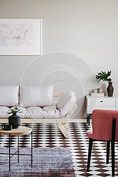 Pastel pink armchair and beige scandinavian futon in trendy living room interior with black and white floor