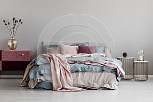 Pastel pink, beige and blue bedding on king size bed in trendy bedroom interior, copy space on empty grey wall