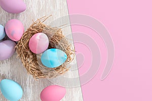 Pastel pink and blue easter eggs in nest with pink paper split background for copy space