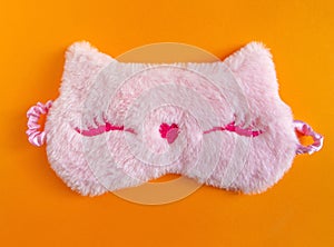 Pastel pink fluffy fur sleep mask with small ears on pastel yellow paper background. Top view, flat lay. Concept of vivid dreams.